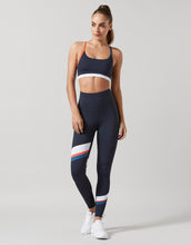 Woman wearing navy sports bra and leggings with colorful stripes on a light gray background