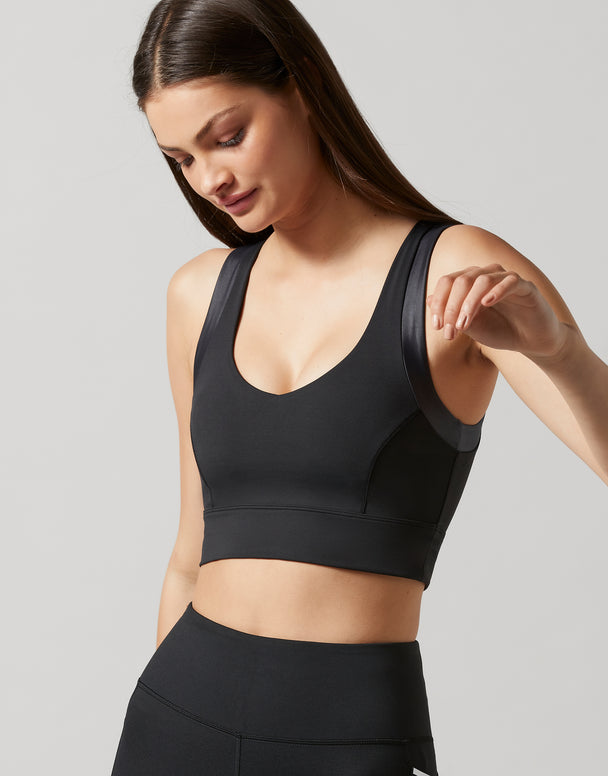 A woman wearing a black athletic sports bra and matching black high-waisted leggings, photographed against a light gray studio background.