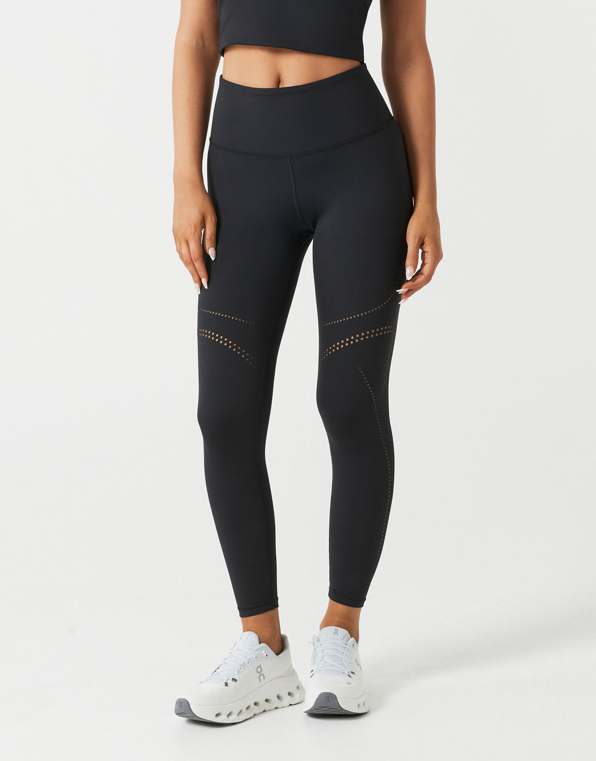 A woman wearing black leggings and white shoes on a white background.