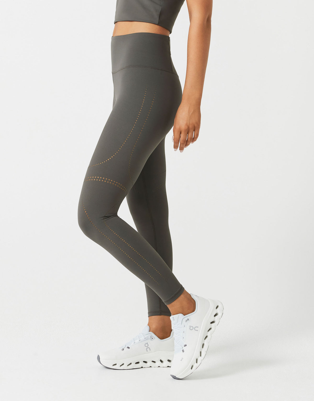 Person wearing gray leggings with white sneakers on a light gray background