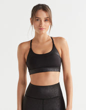 Woman wearing a black sports bra and leggings on a light gray background