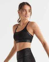 Woman wearing a black sports bra and leggings on a light gray background