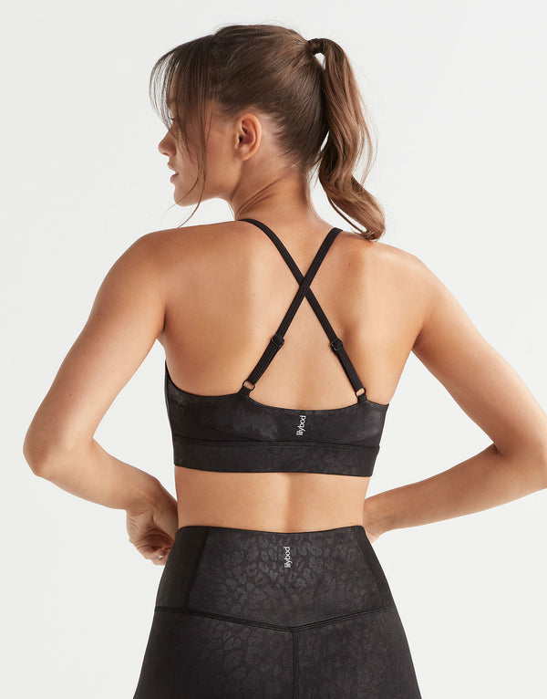 Woman wearing a black sports bra and leggings on a light gray background