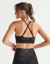 Woman wearing a black sports bra and leggings on a light gray background