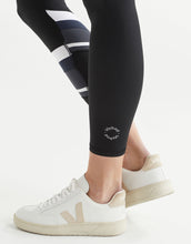 Person wearing black leggings with a logo and white sneakers on a white background