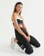Woman wearing a black, white and gray sports bra and leggings on a white background