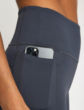 Dark gray leggings with a pocket holding a smartphone on a neutral background