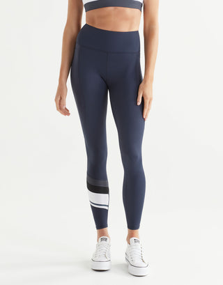 Woman wearing navy leggings with a white stripe on a light gray background