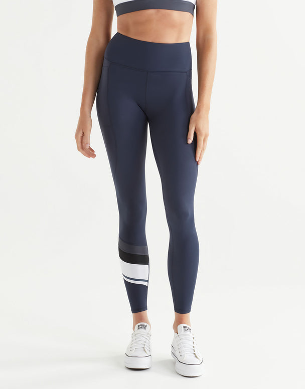 Woman wearing navy leggings with a white stripe on a light gray background
