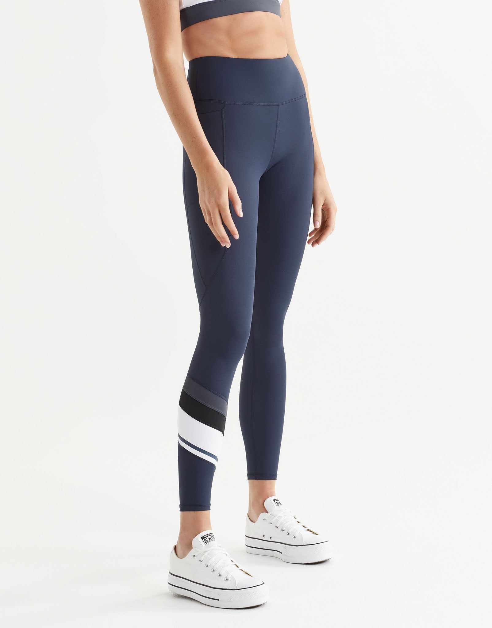 Woman wearing navy leggings with a white stripe on a white background