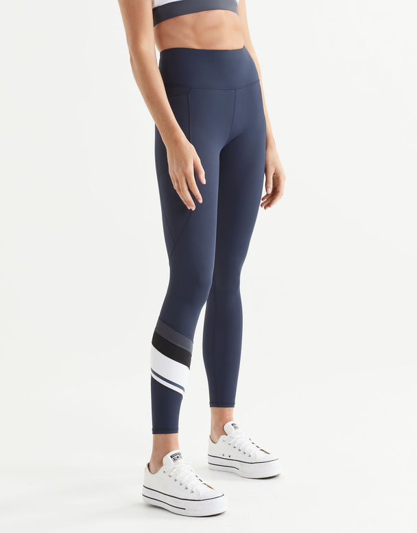 Woman wearing navy leggings with a white stripe on a white background