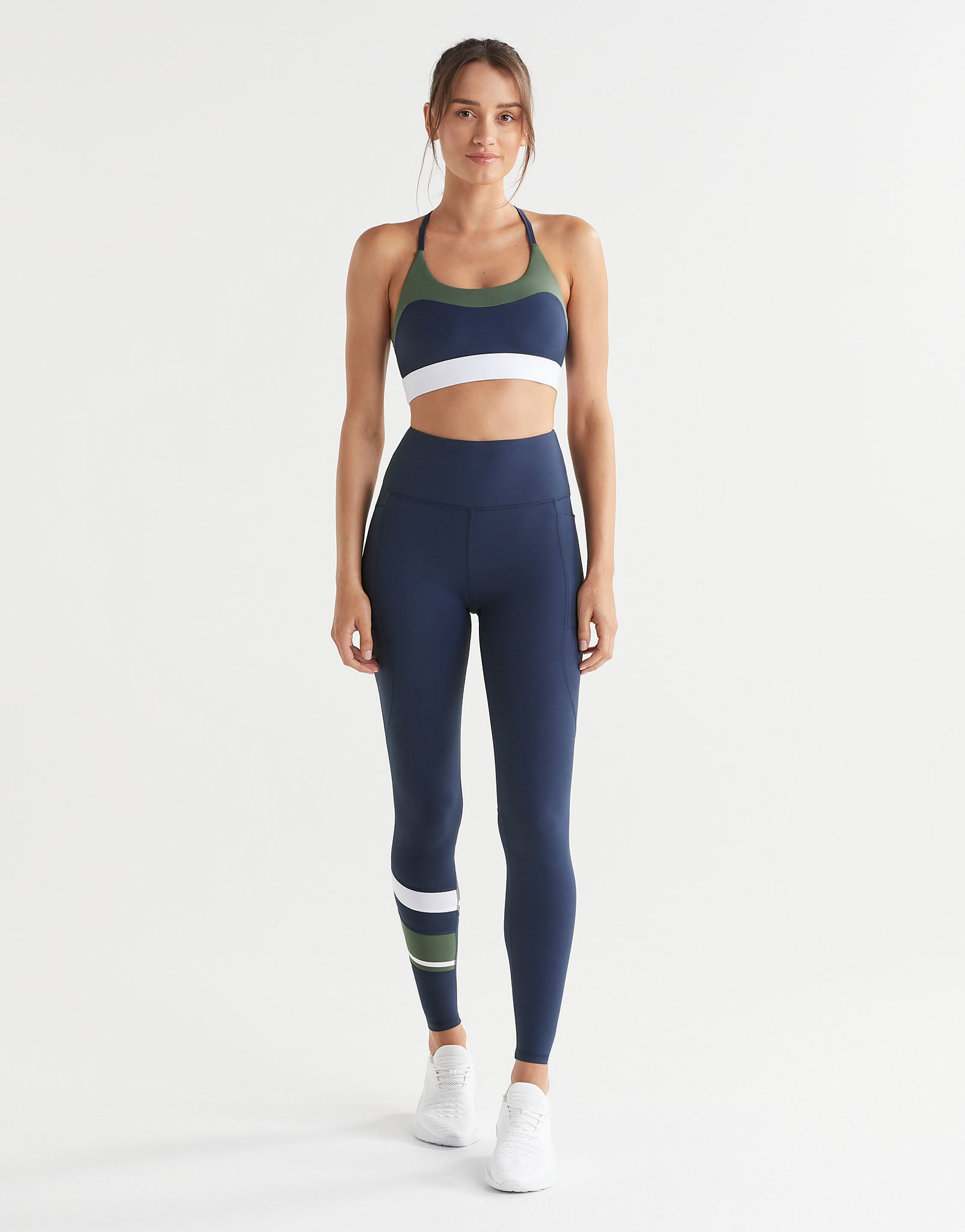 Woman wearing a navy sports bra and leggings with colour blocking on a white background
