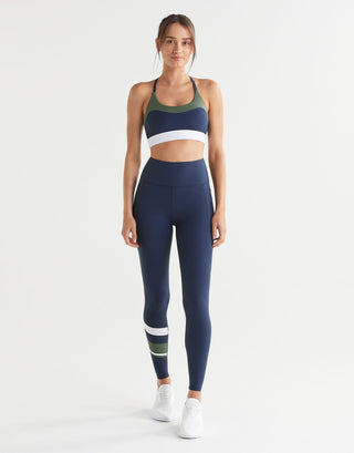 Woman wearing a navy sports bra and leggings with colour blocking on a white background