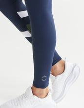 Navy leggings with white stripes worn by a person, paired with white sneakers on a light gray background.