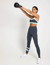 Woman in athletic wear lifting a black kettlebell against a white background