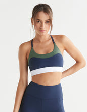 Woman wearing a  navy blue and green sports bra and leggings with a white background
