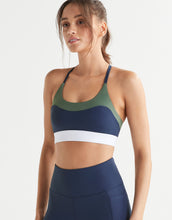 Woman wearing a navy blue and green sports bra and navy leggings with a white background