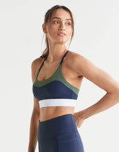 Woman wearing a navy blue and green sports bra and leggings on a white background