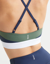 Close up of a green and navy sports bra with white waistband on a plain background