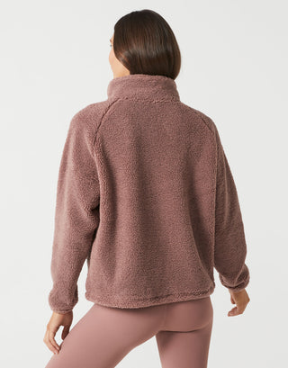 A woman shown from the back wearing a dusty rose fleece pullover and matching leggings against a clean light gray studio background.