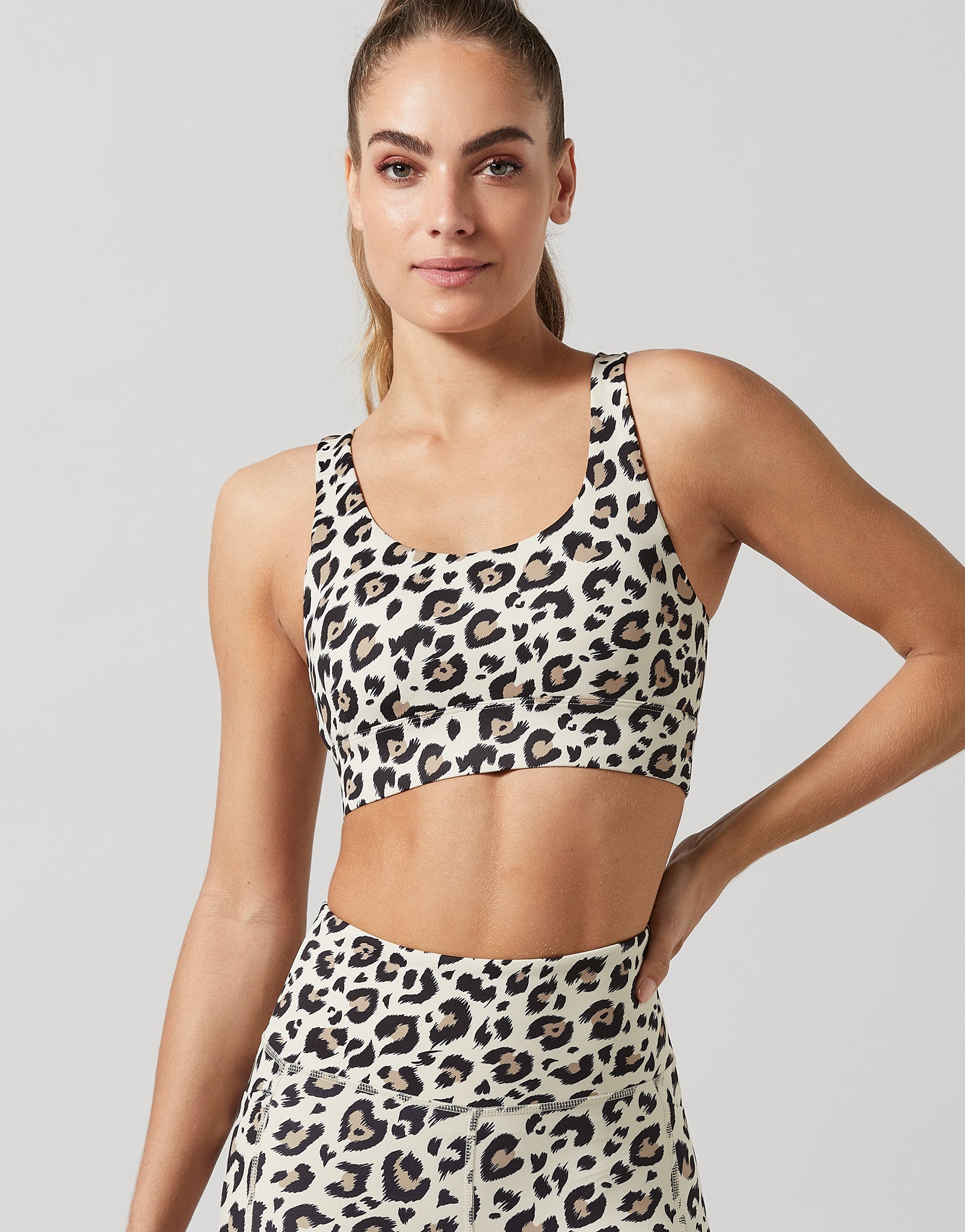 Woman wearing a leopard print sports bra and leggings on a plain background