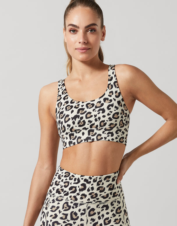 Woman wearing a leopard print sports bra and leggings on a plain background