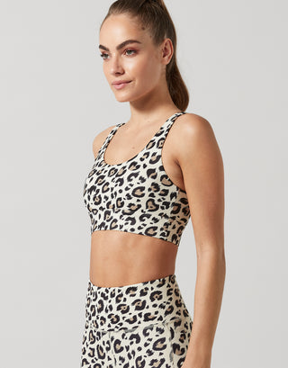 Woman wearing a leopard print sports bra and leggings on a plain background