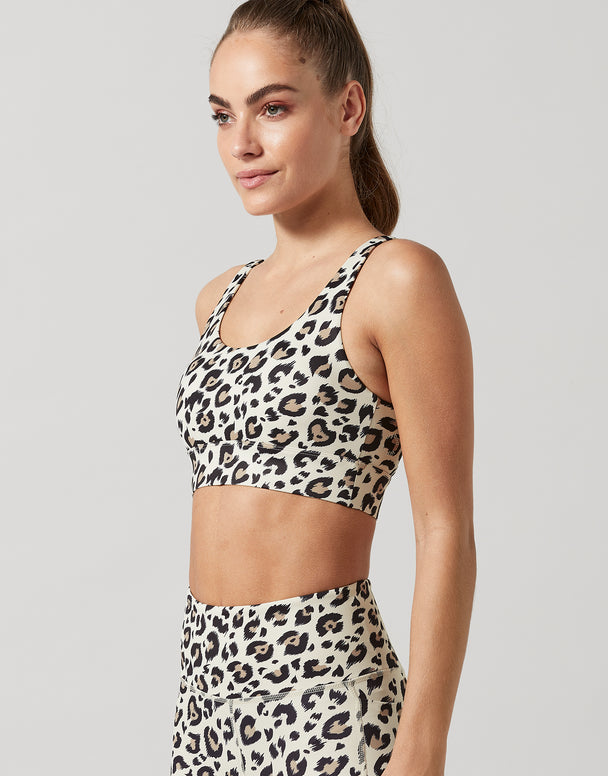 Woman wearing a leopard print sports bra and leggings on a plain background