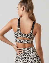 Woman wearing a leopard print sports bra and shorts on a plain background
