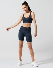 A woman wearing blue leopard print bike shorts and sports bra.