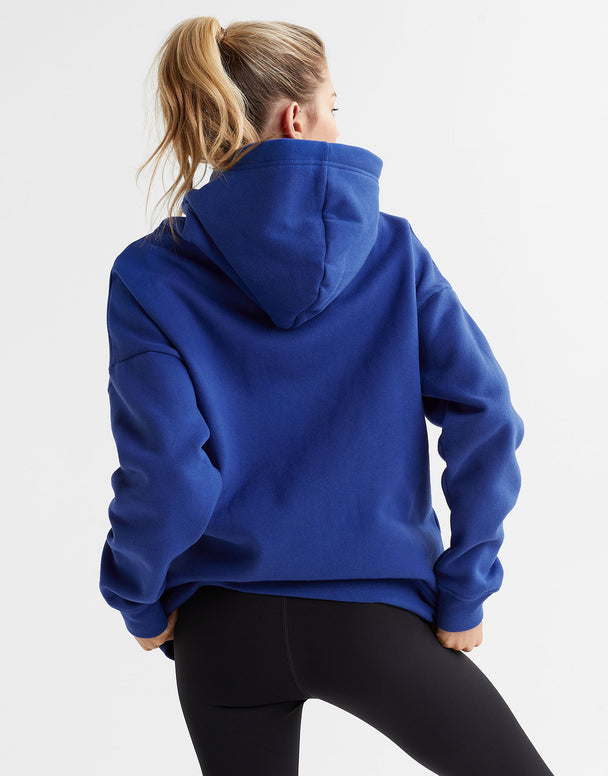 A woman wearing a blue hooded fleece sweater with a kangaroo pocket and drawstrings on the hood. The sweater is oversized.