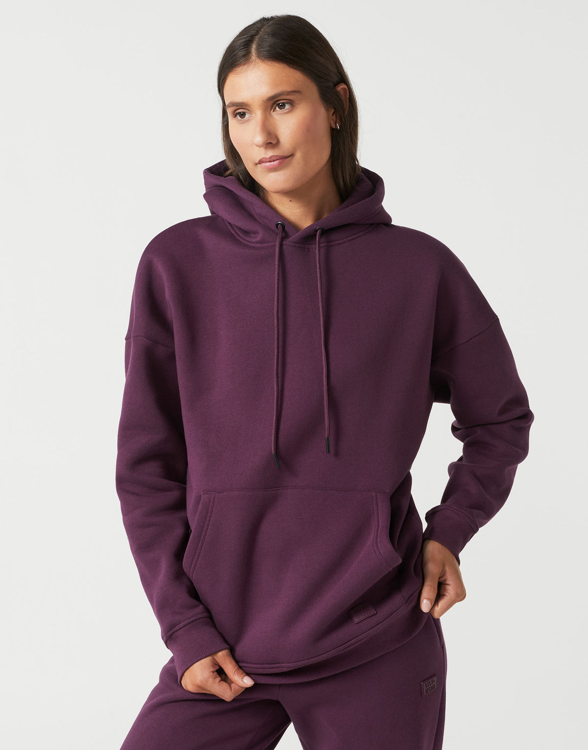 A woman modeling a matching deep purple sweatshirt and jogger pants set against a clean, light gray studio background.