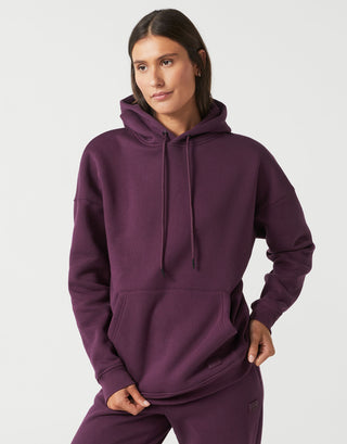 A woman modeling a matching deep purple sweatshirt and jogger pants set against a clean, light gray studio background.