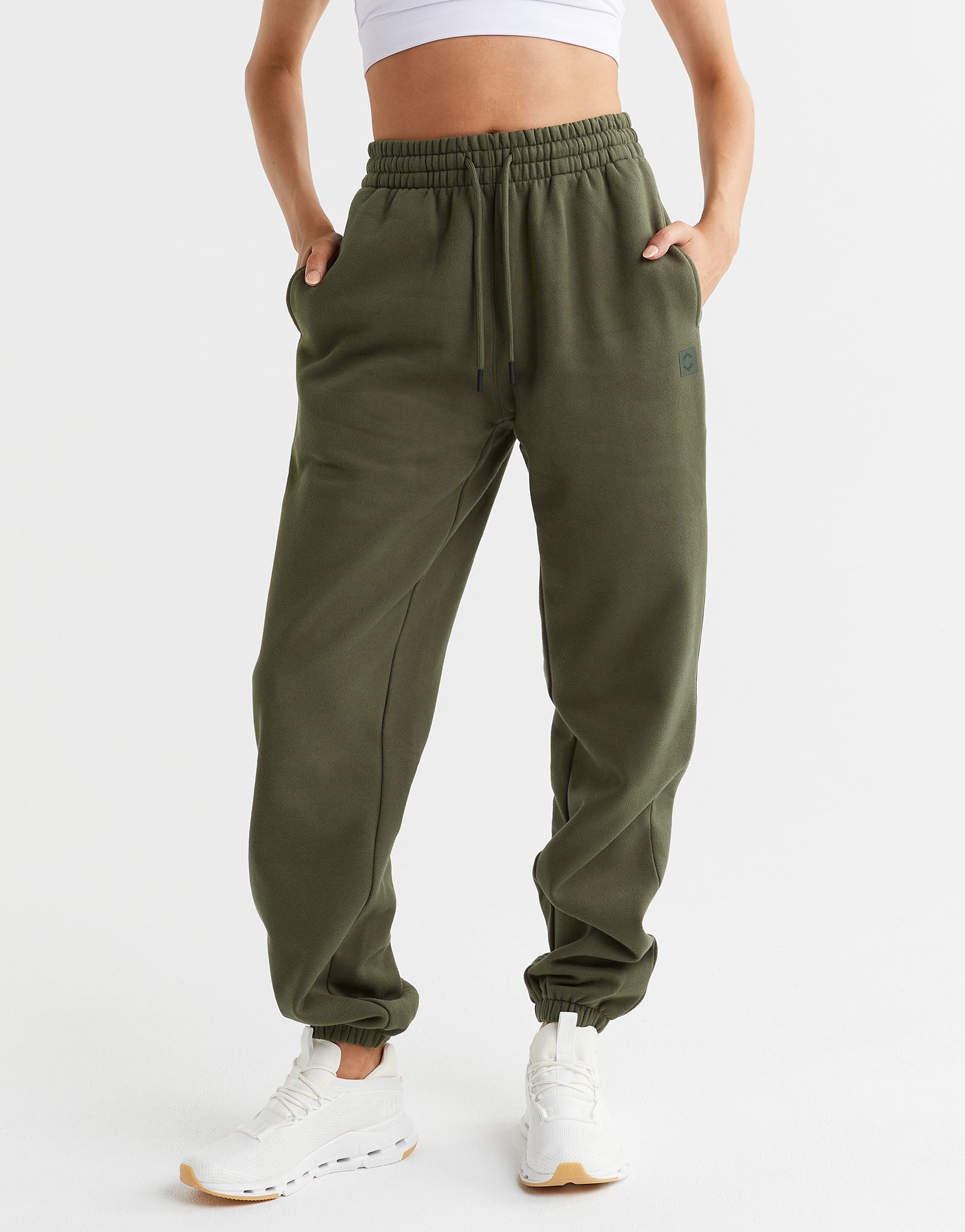 A woman wearing a pair of olive green sweatpants and white runners.