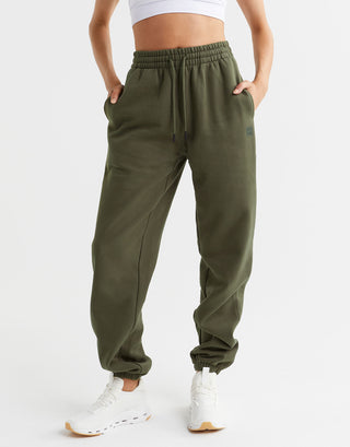 A woman wearing a pair of olive green sweatpants and white runners.