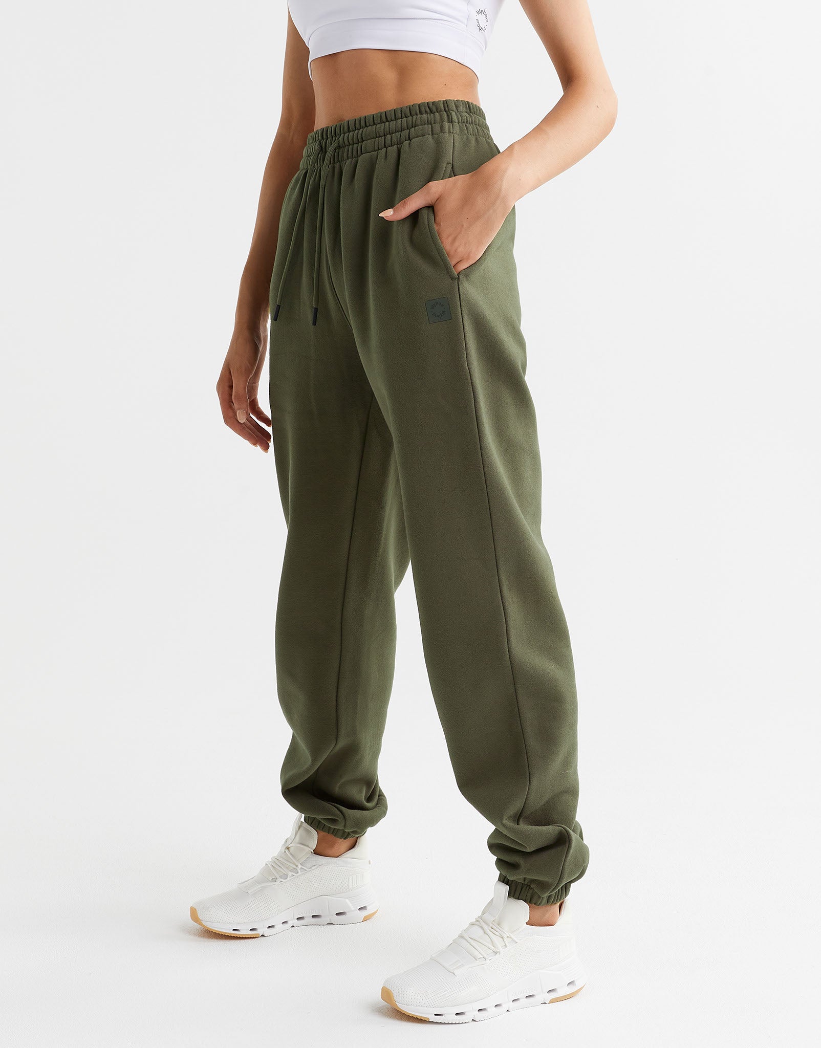 A model wearing a pair of olive green sweatpants and white runners.
