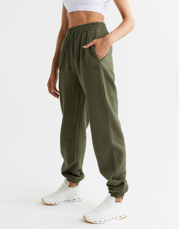 A model wearing a pair of olive green sweatpants and white runners.