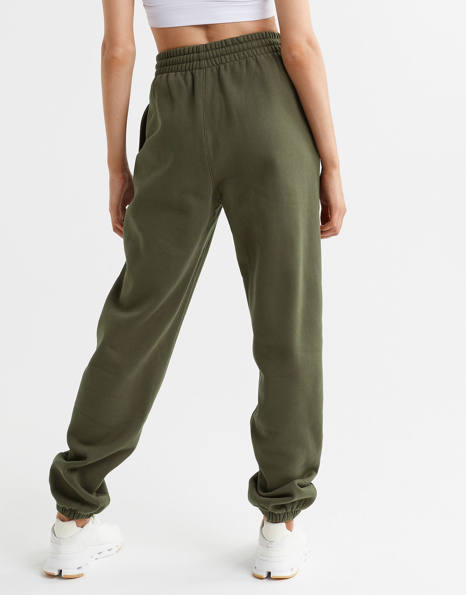 A woman wearing a pair of olive green sweatpants, a white top and white runners.