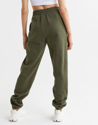 A woman wearing a pair of olive green sweatpants, a white top and white runners.