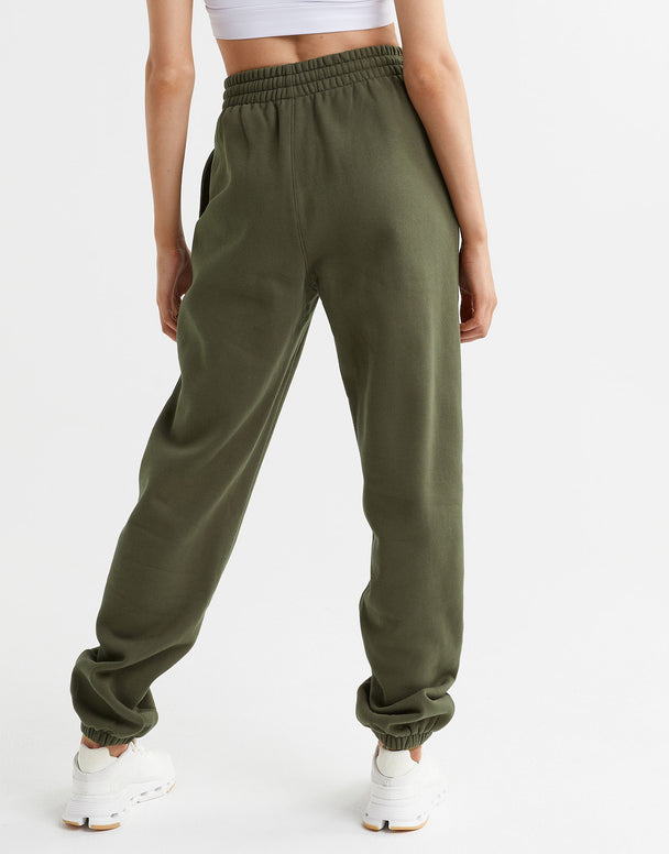 A woman wearing a pair of olive green sweatpants, a white top and white runners.