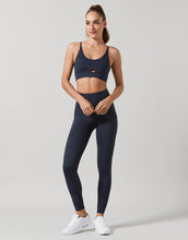 Woman wearing a navy Lilybod sports bra and leggings set on a light gray background