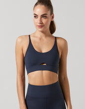Woman wearing a navy blue sports bra and leggings on a light gray background