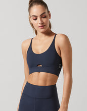 Woman wearing a navy blue Lilybod sports bra and leggings on a light gray background