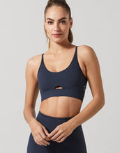 Woman wearing a navy blue Lilybod sports bra and leggings on a light gray background - Holistic Femme