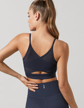 Woman wearing a navy blue Lilybod sports bra and leggings on a light gray background