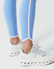 Light blue leggings with white trim worn by a person, paired with white sneakers on a light gray background.