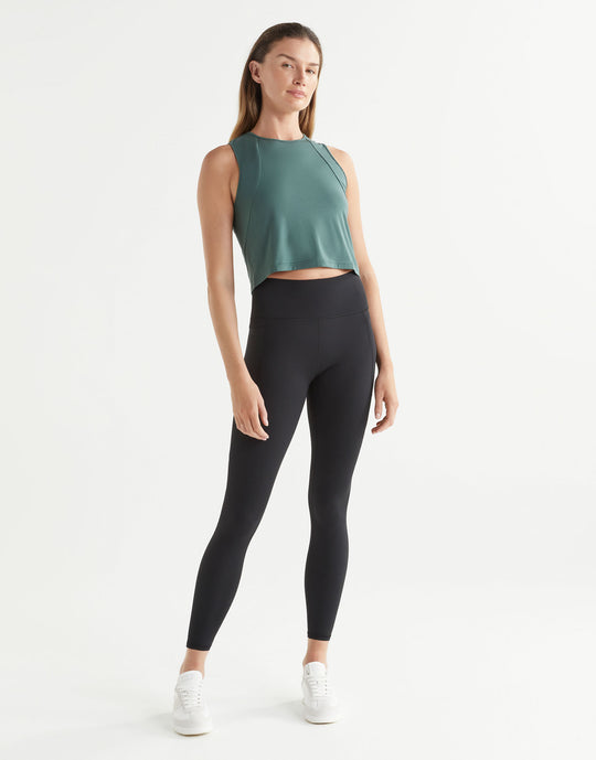Woman wearing a green sleeveless top and black leggings on a white background