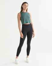 Woman wearing a green sleeveless top and black leggings on a white background