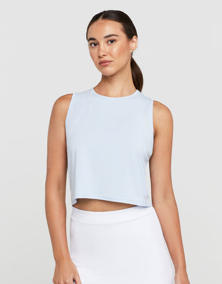 Woman wearing a light blue sleeveless top and white pants on a plain background