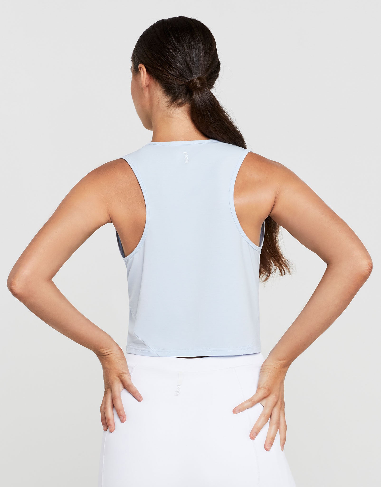 Woman wearing a light blue sleeveless top and white pants on a plain background
